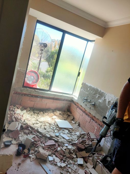 Photo showing where the bath had been. Tiles stripped of the walls and lots of rubble on the floor. Extraction fan at the window to remove most of the dust